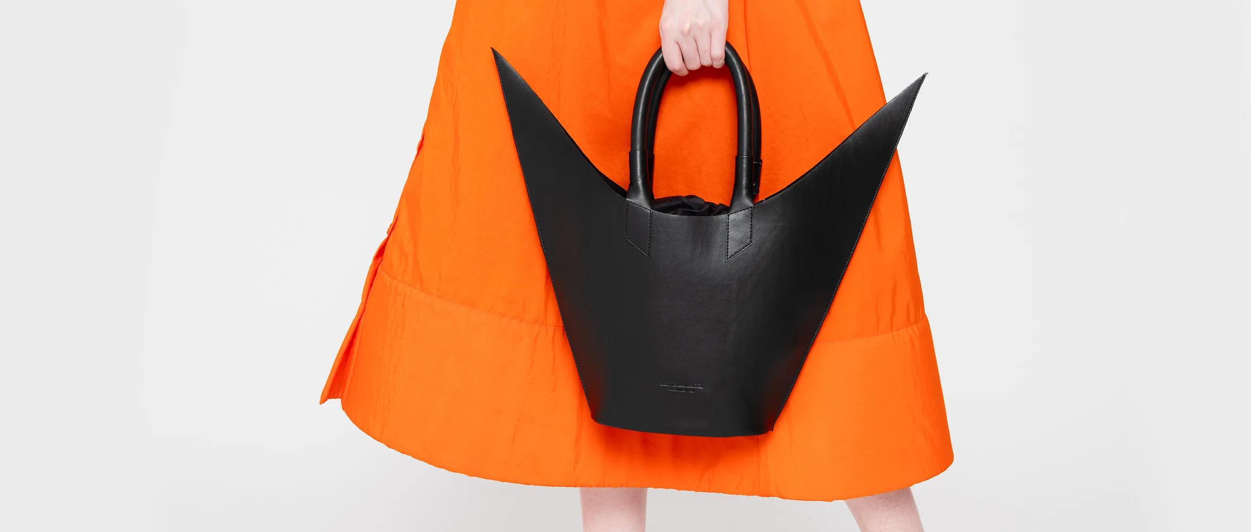 Woman in Orange dress holding pointy black pleather bag