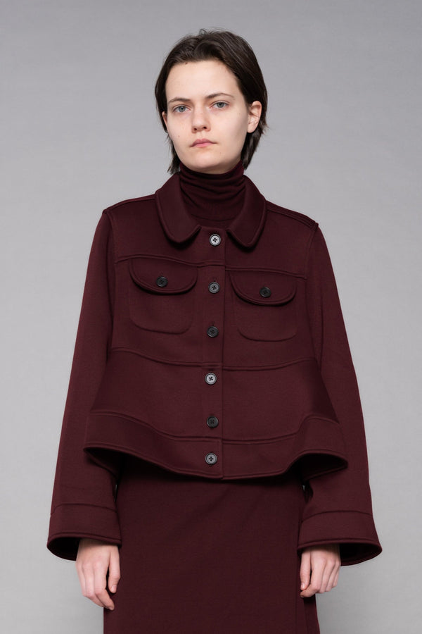 Person wearing a burgundy outfit with a jacket and skirt on a gray background