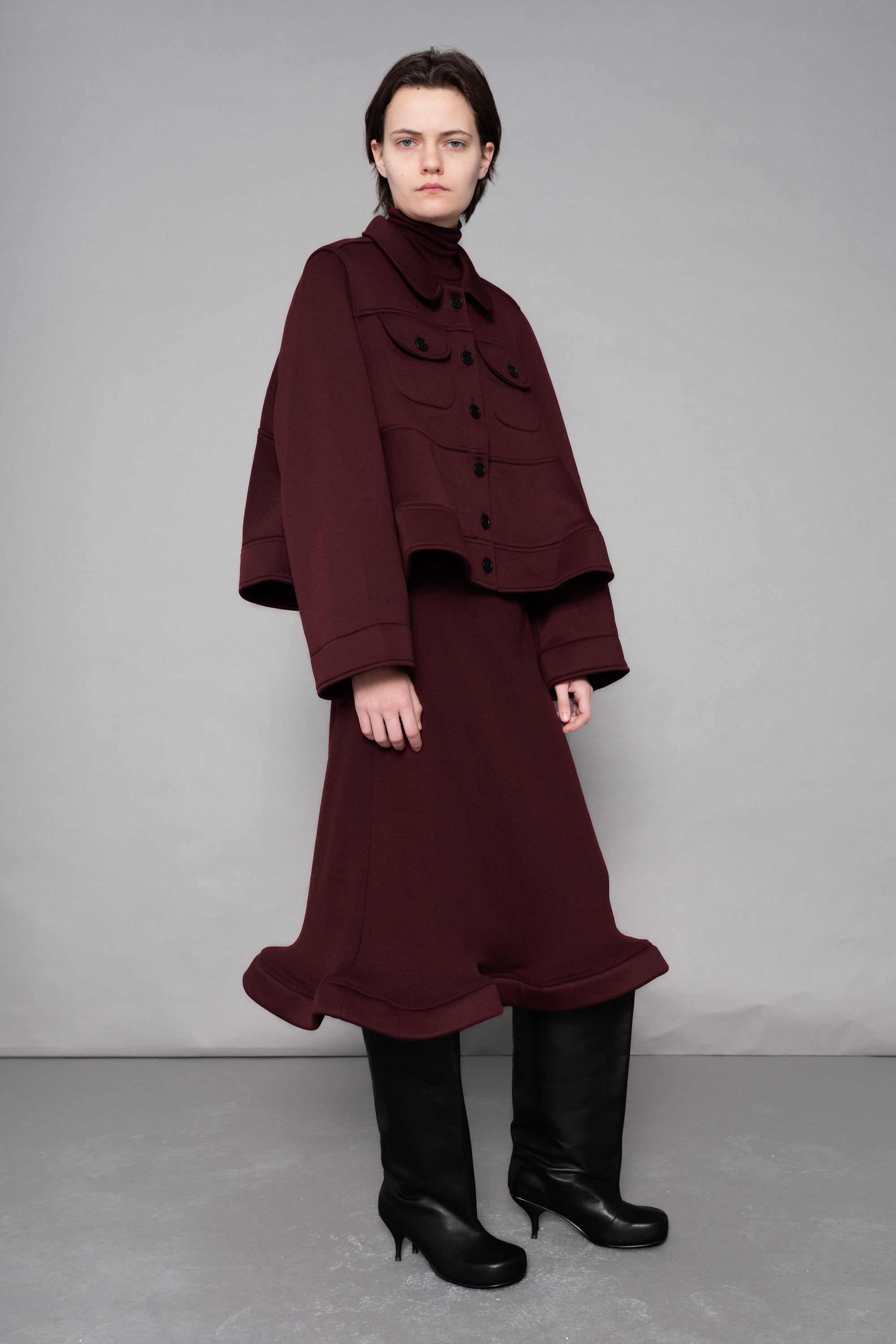 Person wearing a burgundy outfit with a coat and skirt against a plain background
