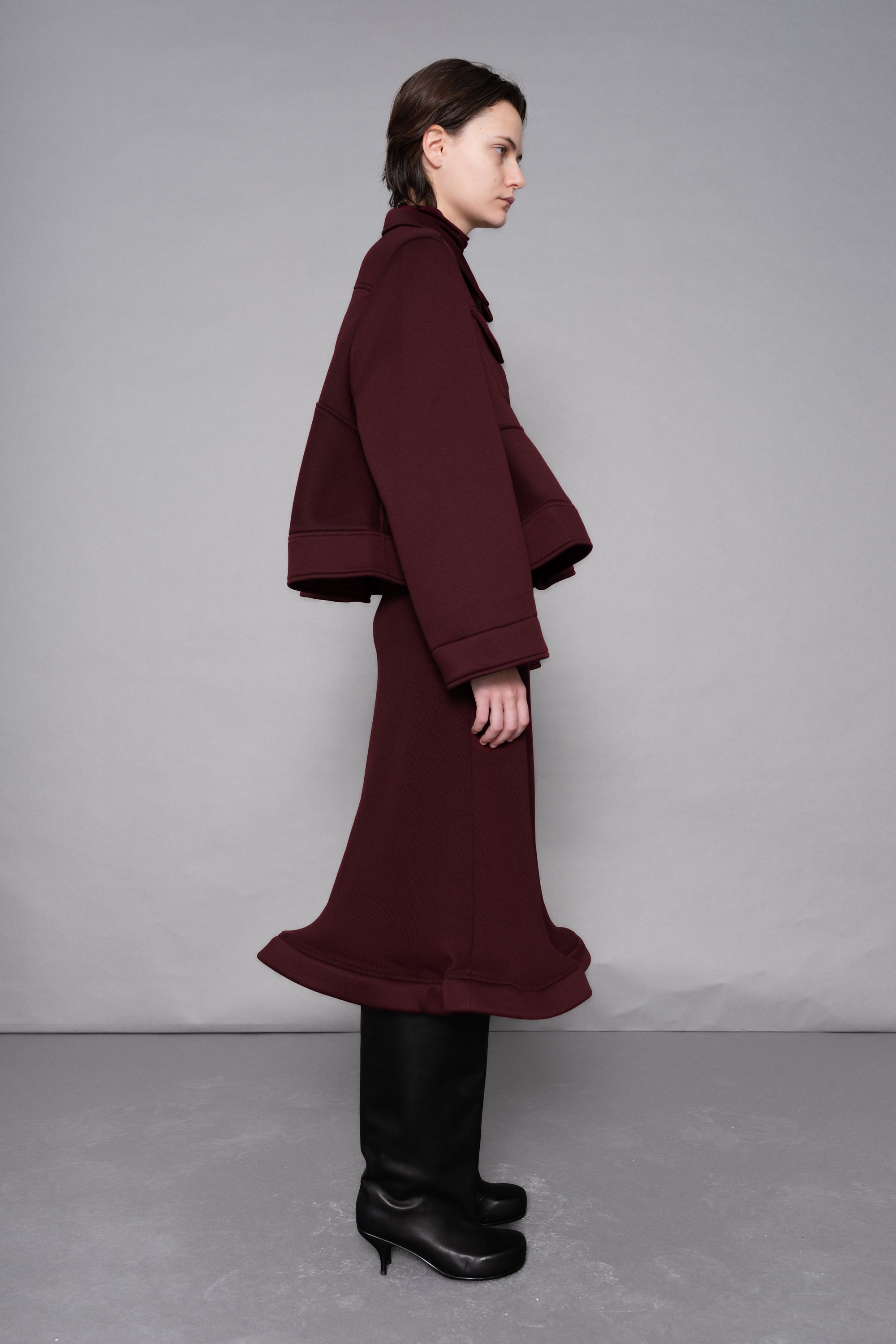 Person wearing a burgundy coat and skirt set against a plain background