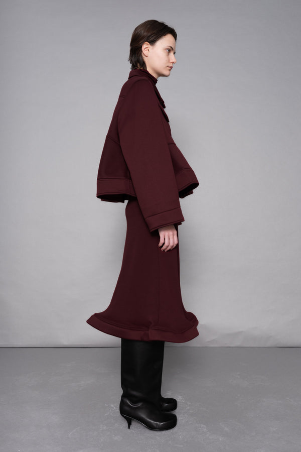 Person wearing a burgundy coat and skirt set against a plain background