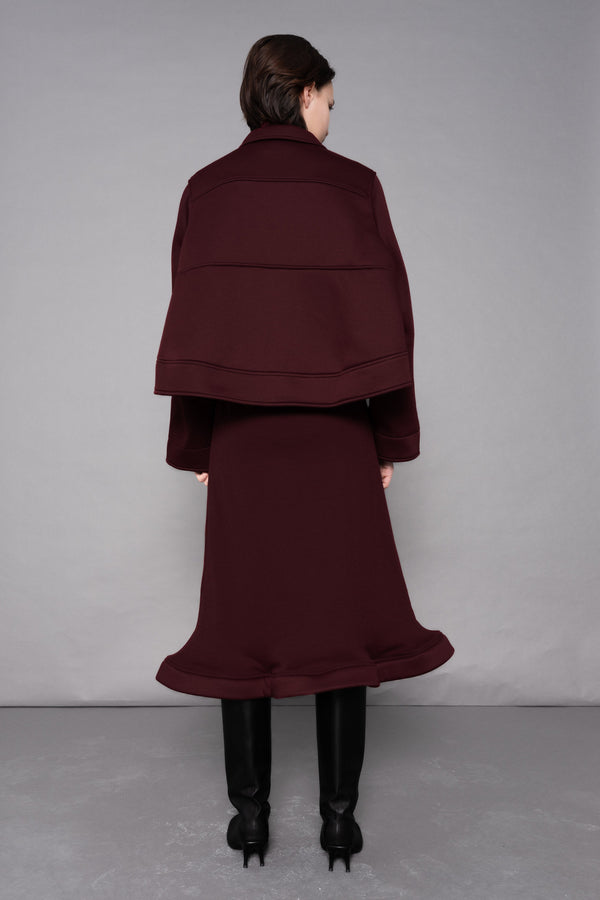 Person wearing a burgundy coat and skirt set against a plain background