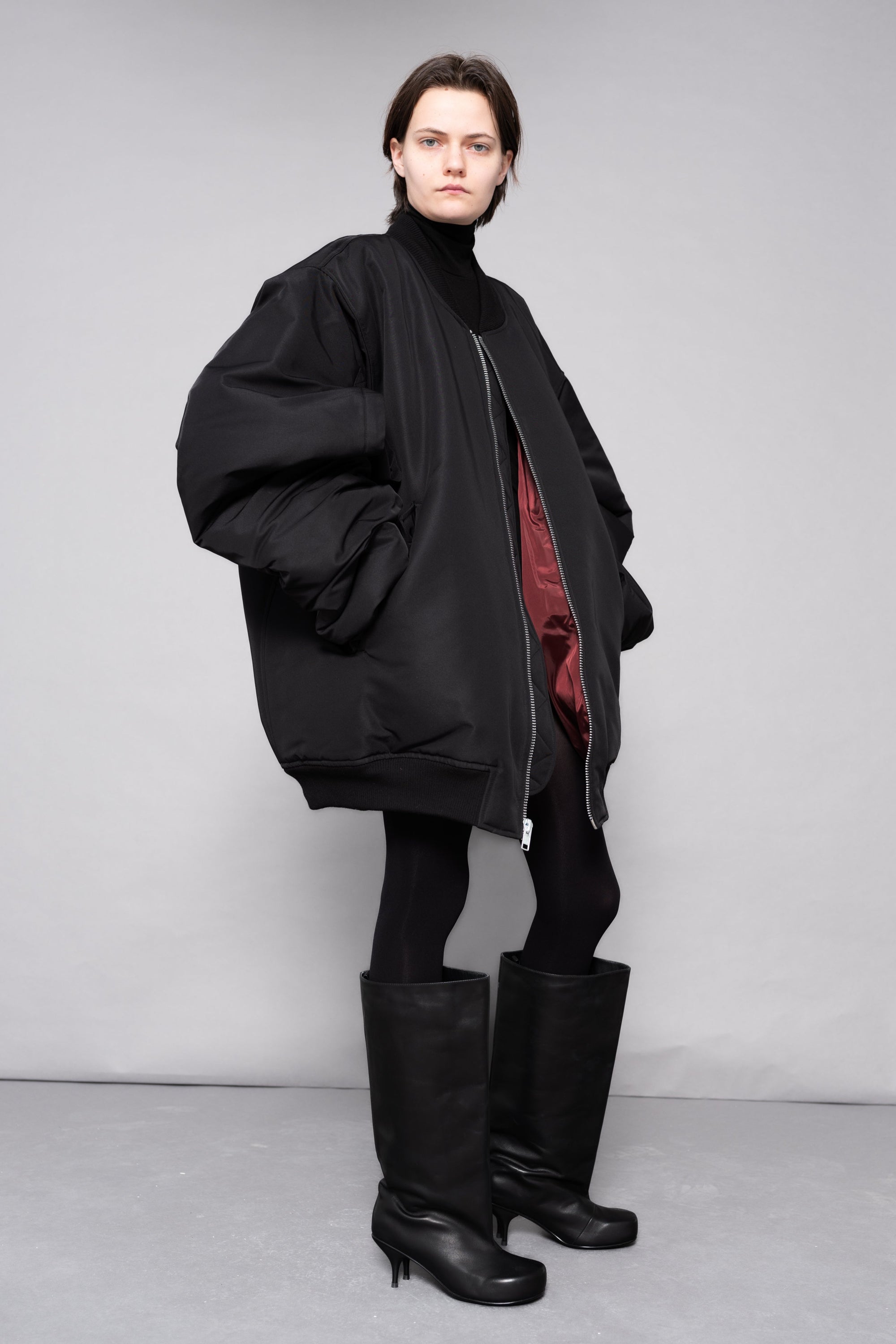 Person wearing a black outfit with a red lining, standing against a plain background