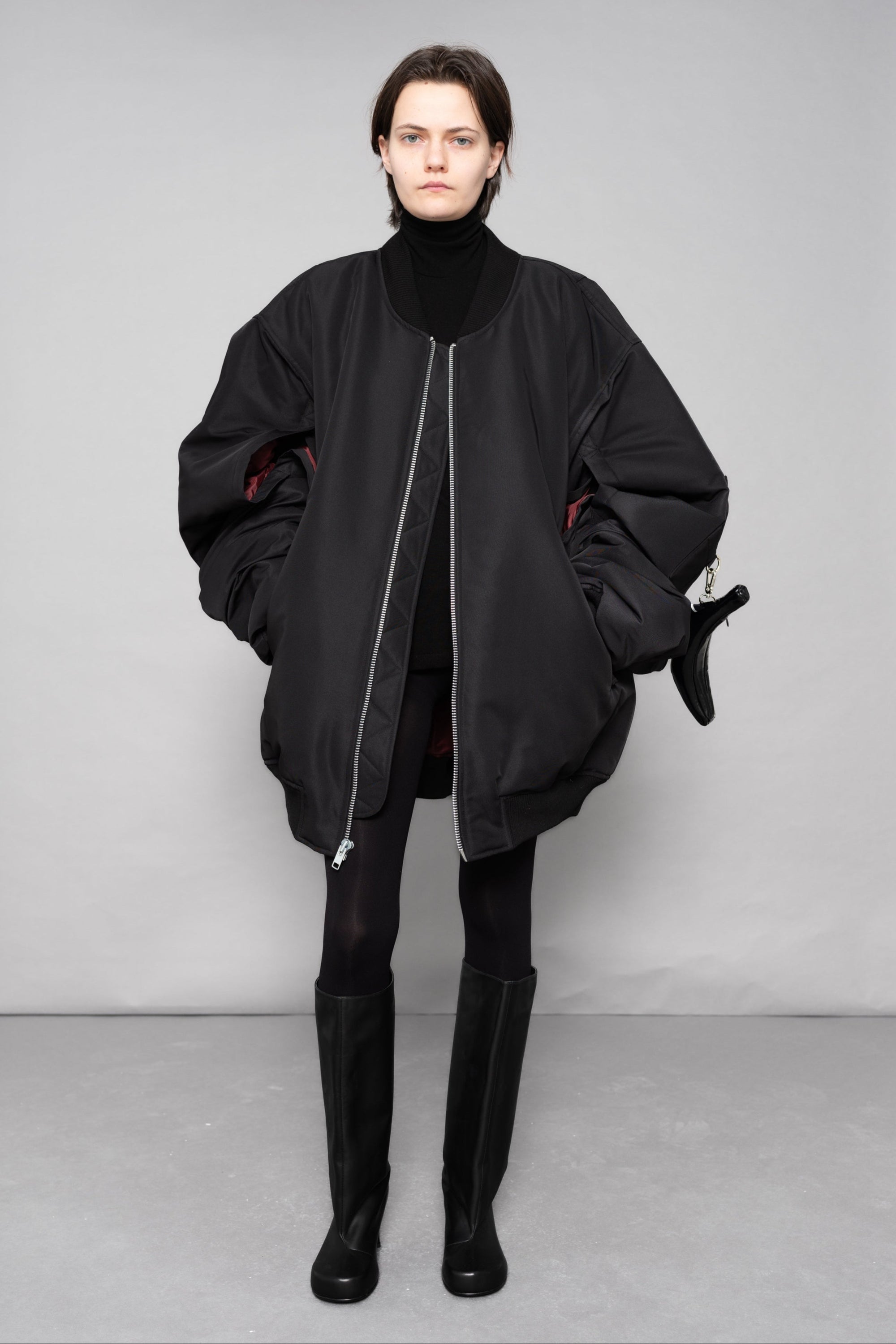 Person wearing a black outfit with a large jacket against a gray background