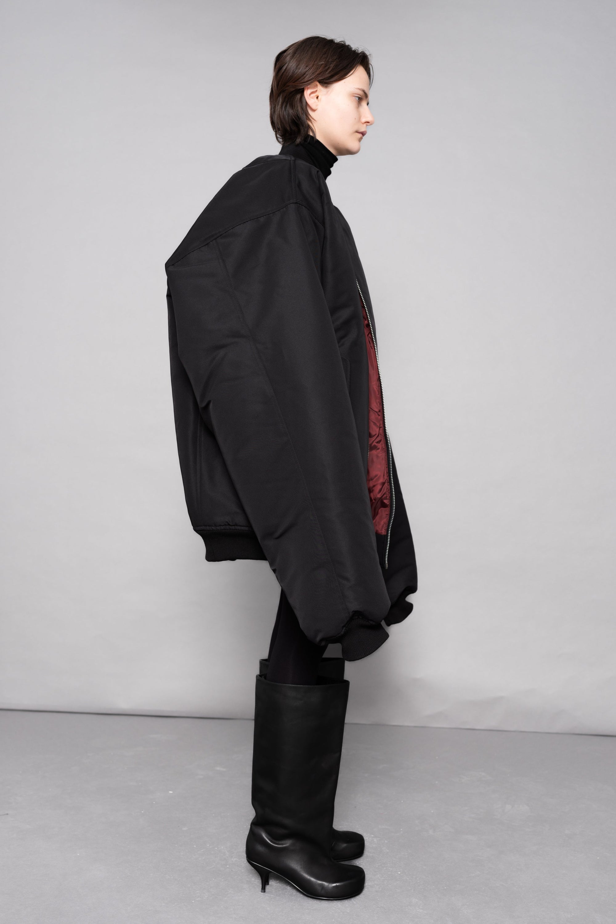 Person wearing a black coat and high boots on a plain background