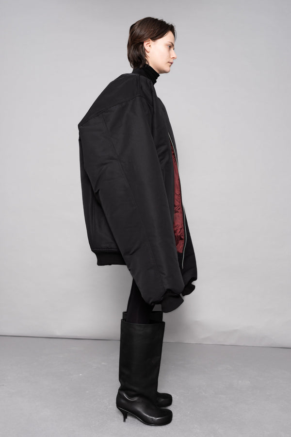 Person wearing a black coat and high boots on a plain background
