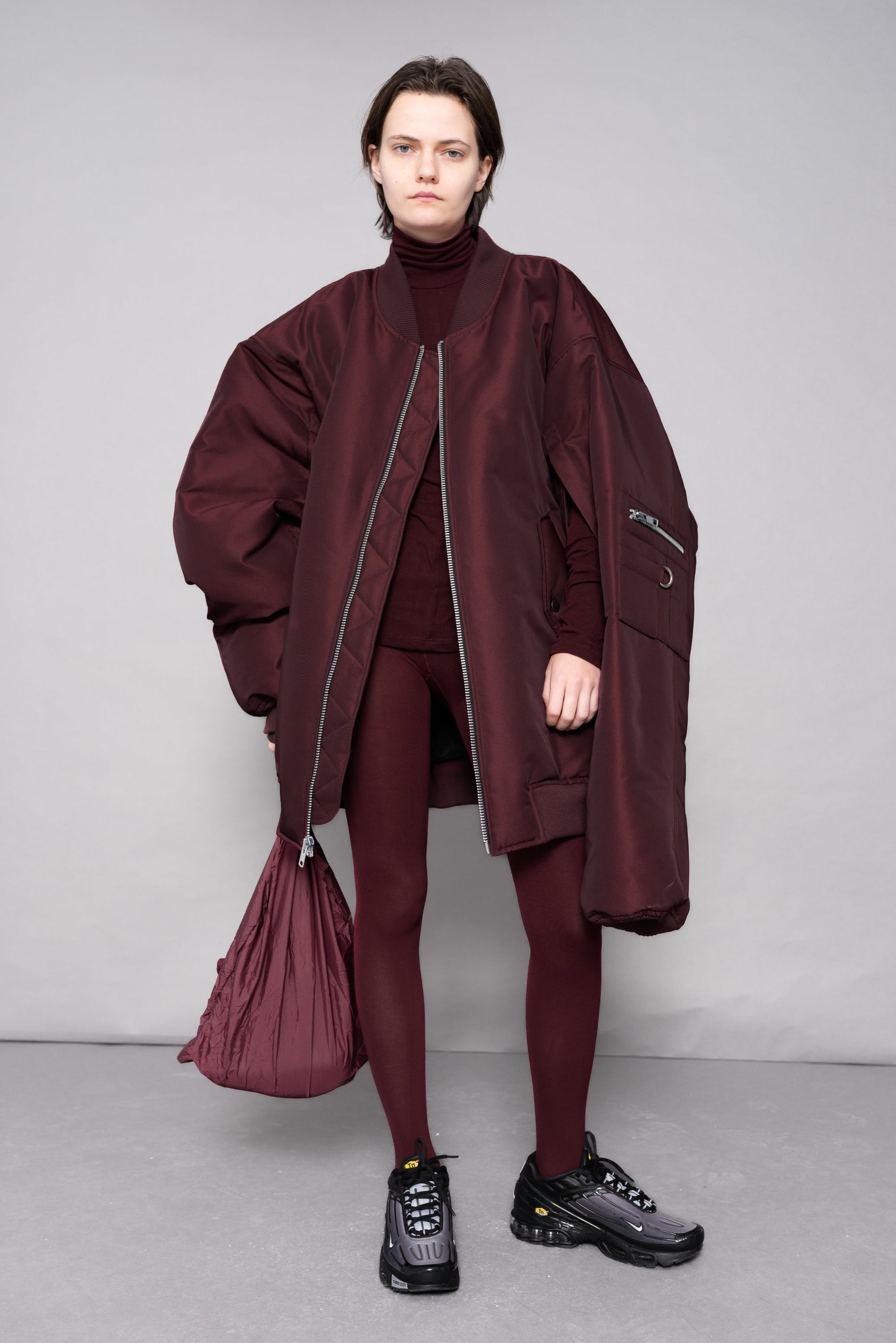 Person wearing a maroon outfit with a matching bag against a plain background