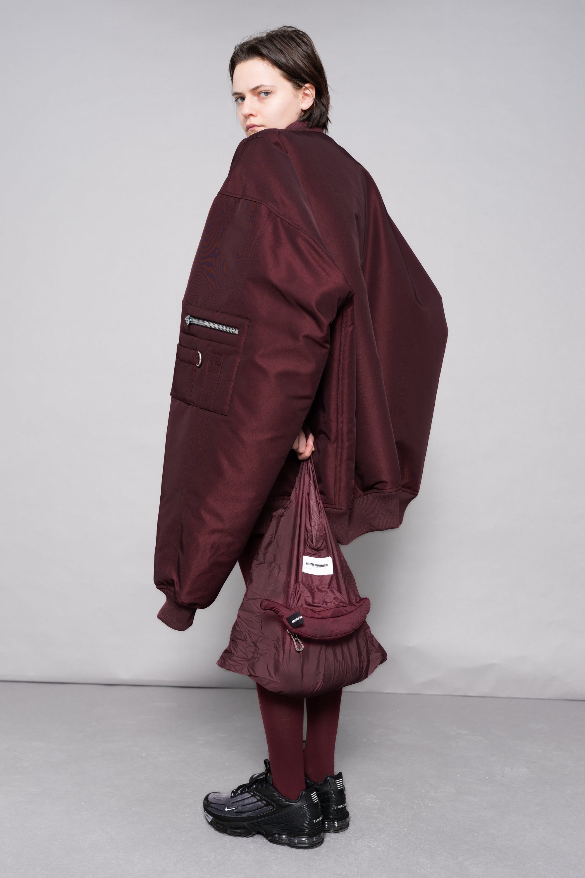 Person wearing a burgundy outfit with a matching bag against a gray background