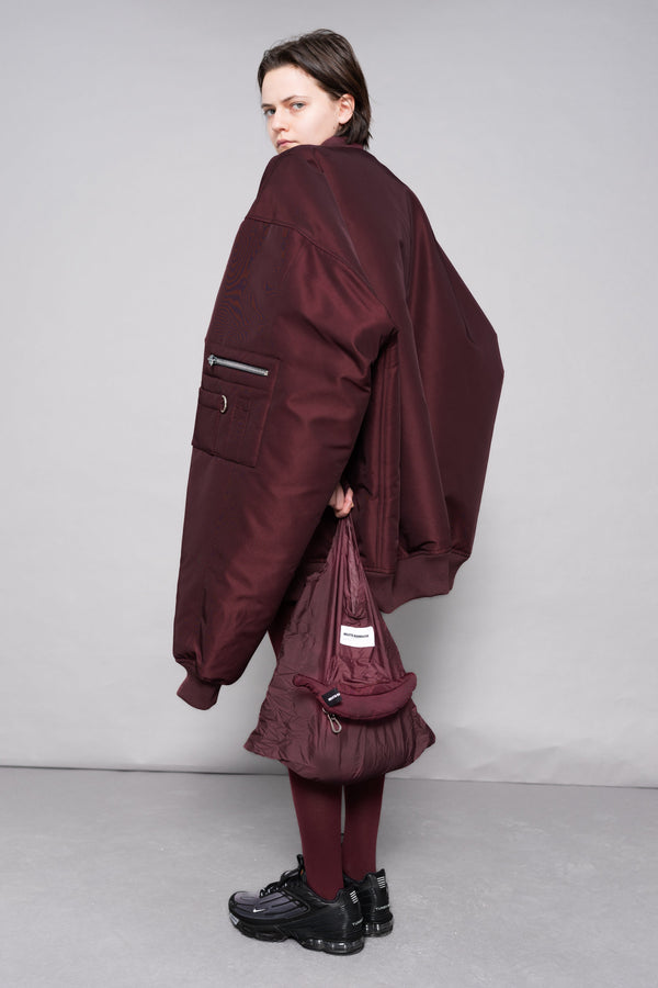 Person wearing a burgundy outfit with a matching bag against a gray background