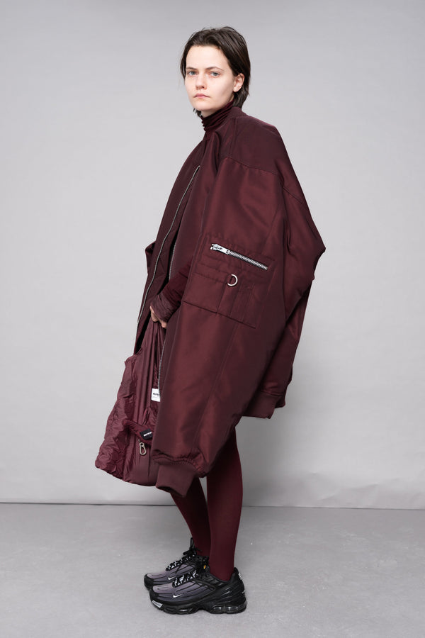Person wearing a long burgundy coat on a plain background