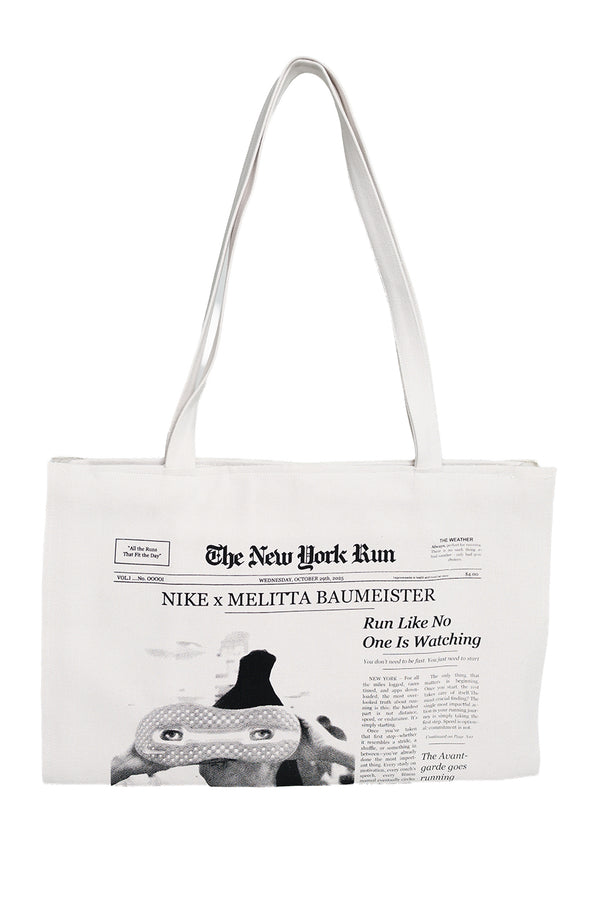A white canvas tote bag featuring a black-and-white newspaper-style print with the headline 'The New York Run' and 'Nike x Melitta Baumeister.' The bag has two long handles and is photographed against a plain white background.