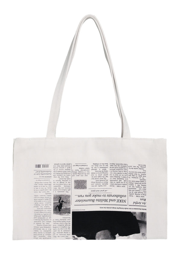 A white canvas tote bag with long shoulder straps, featuring a printed collage of newspaper columns and images on the front.