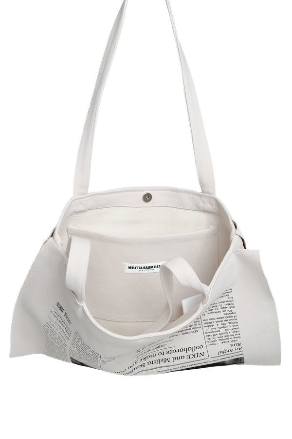 An off-white canvas shoulder bag with a newspaper print pattern on the lower front and a small white label that reads MELITTA BAUMEISTER