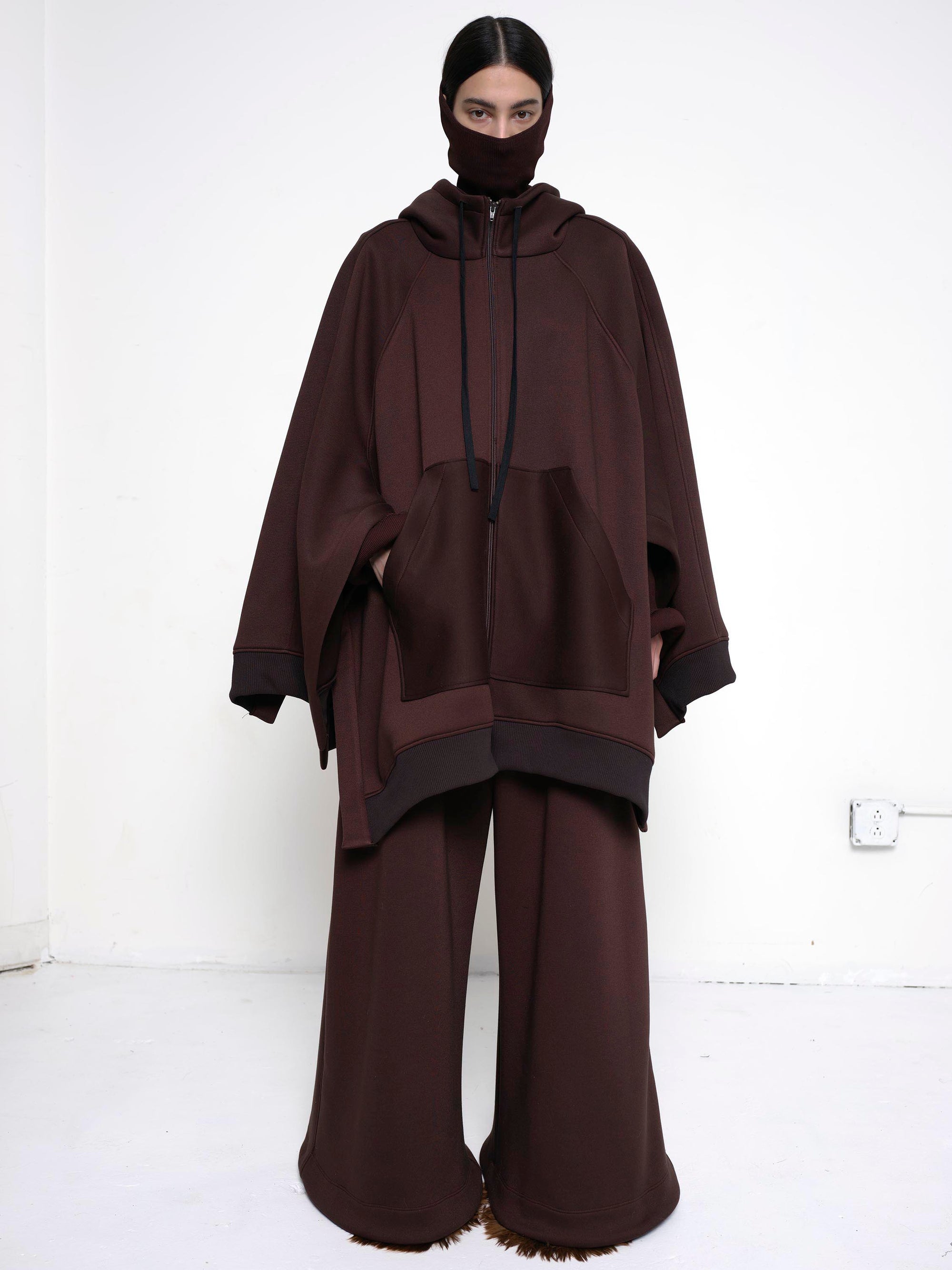BRUNETTE-WOMAN-LOOKING-STRAIGHT-CAMERA-WEARING-BIG-ZIP-UP-HOODIE-BROWN-AND-TURTLENECK-ABOVE-NOSE-FULL-BODY-SHOT