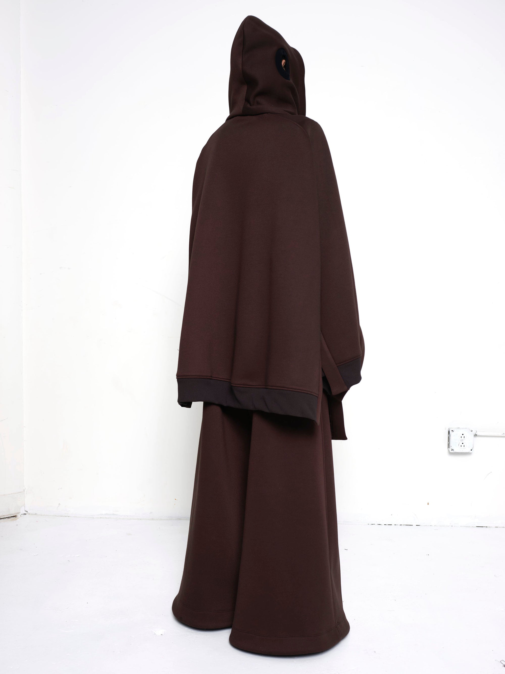 BRUNETTE-WOMAN-FROM-BACK-WEARING-BIG-ZIP-UP-HOODIE-BROWN-AND-TURTLENECK-ABOVE-NOSE-FULL-BODY-IMAGE-BROWN-PANTS-HOOD-ON