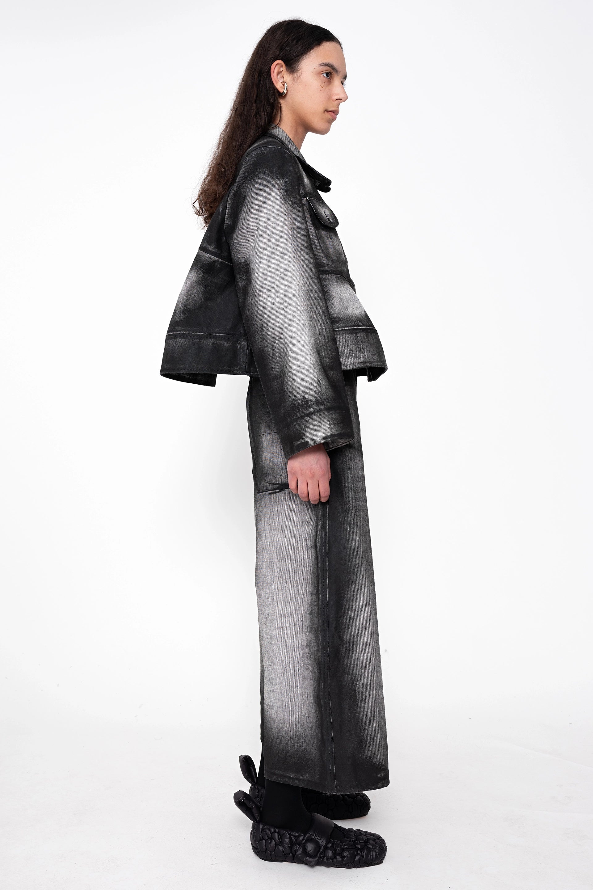 female-wearing-black-and-white-spray-painted-cropped-denim-shirt-with-foam-detail-at-hem-with-matching-cropped-denim-pants-on-white-background-full-body-side