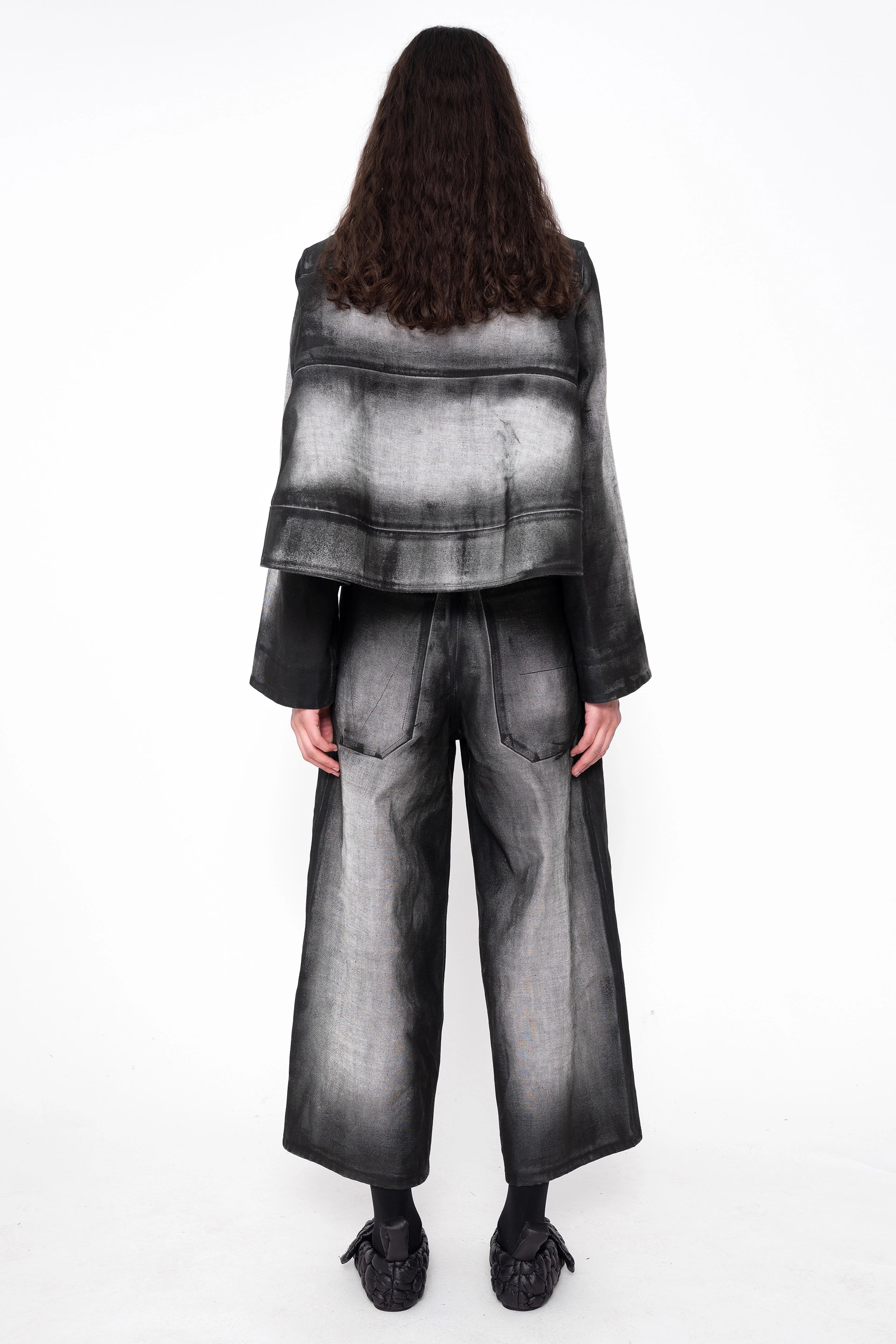 female-wearing-black-and-white-spray-painted-cropped-denim-shirt-with-foam-detail-at-hem-with-matching-cropped-denim-pants-on-white-background-full-body-back