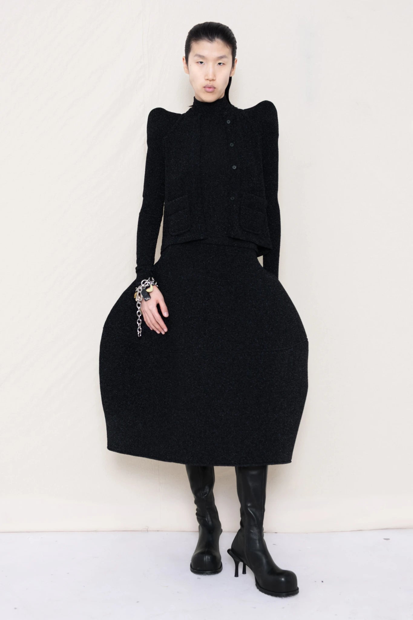 PERSON-WEARING-GLITTER-BLACK-FOAMY-SHOULDER-CARDIGAN-WITH-MATCHING-MOCK-NECK-SHIRT-AND-FOAMY-BALL-SKIRT-WEARING-BLACK-DOUBLE-HEELED-BOOTS-ACCESSORIZED-ON-THE-WRIST-MB-CHARM-BRACELET-FRONT-VIEW