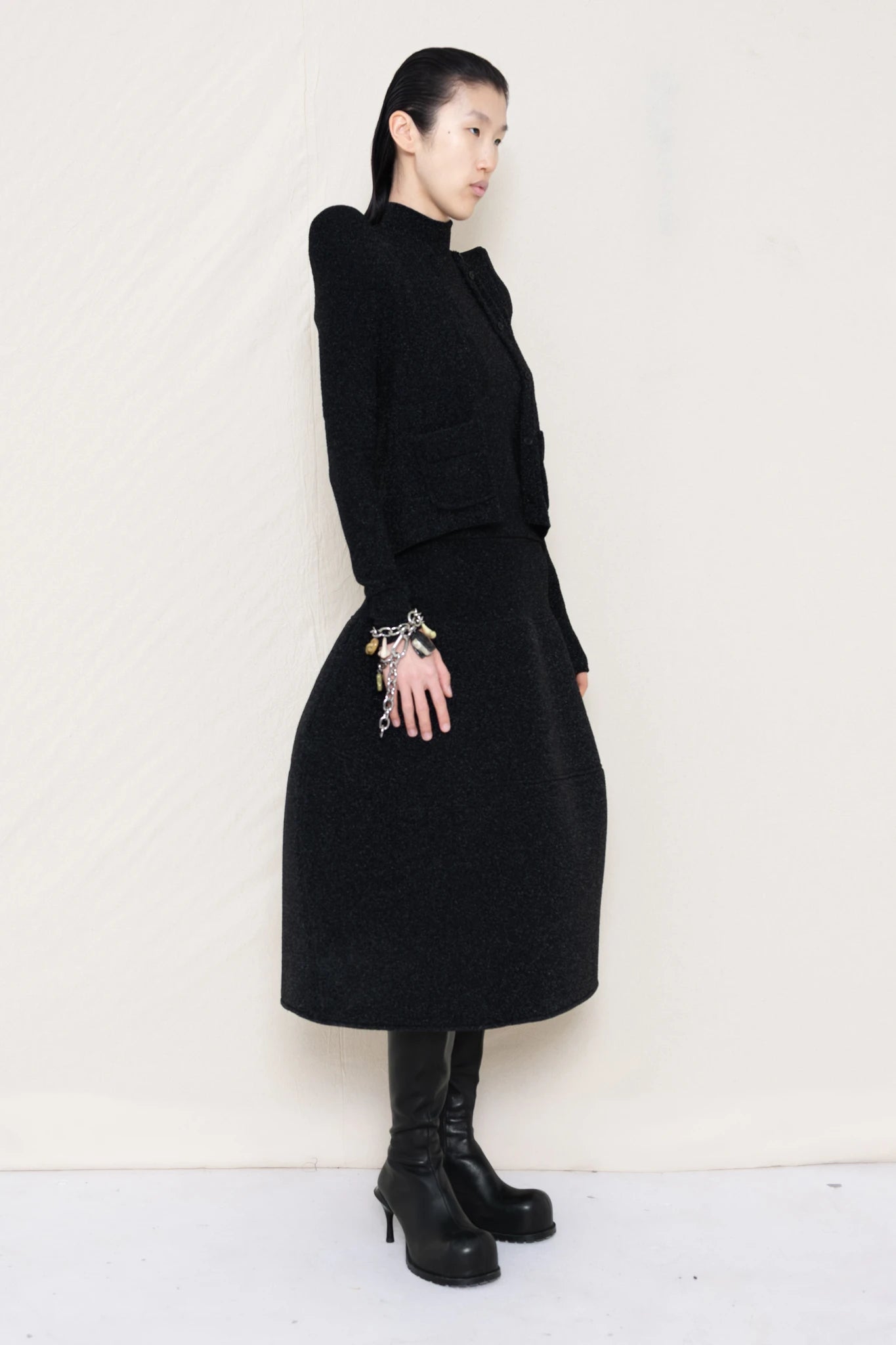 PERSON-WEARING-GLITTER-BLACK-FOAMY-SHOULDER-CARDIGAN-WITH-MATCHING-MOCK-NECK-SHIRT-AND-FOAMY-BALL-SKIRT-WEARING-BLACK-DOUBLE-HEELED-BOOTS-ACCESSORIZED-ON-THE-WRIST-MB-CHARM-BRACELET-THREE-QUARTER-VIEW