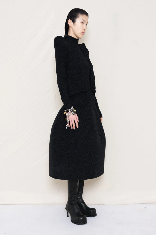 PERSON-WEARING-GLITTER-BLACK-FOAMY-SHOULDER-CARDIGAN-WITH-MATCHING-MOCK-NECK-SHIRT-AND-FOAMY-BALL-SKIRT-WEARING-BLACK-DOUBLE-HEELED-BOOTS-ACCESSORIZED-ON-THE-WRIST-MB-CHARM-BRACELET-THREE-QUARTER-VIEW