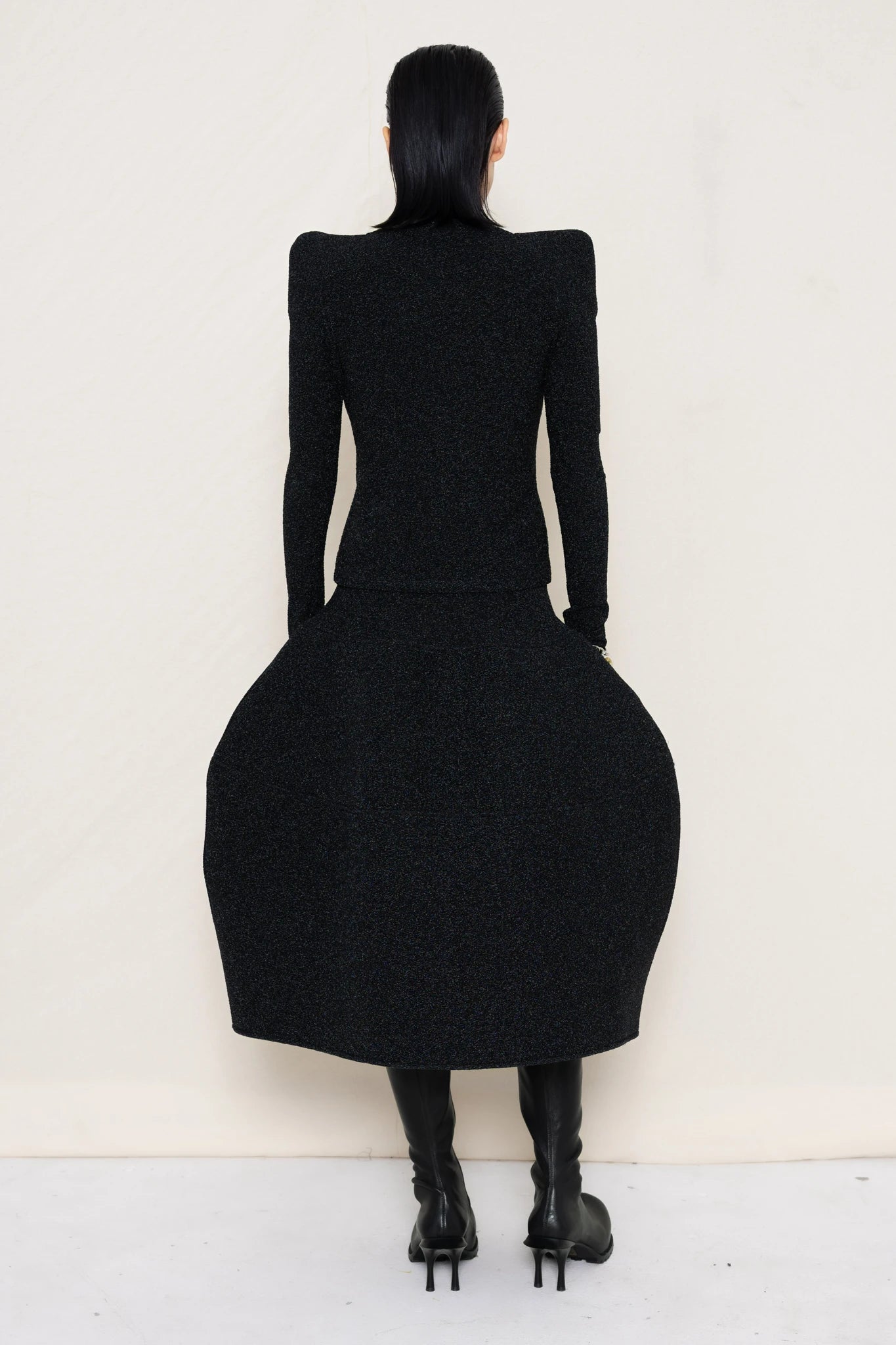 PERSON-WEARING-GLITTER-BLACK-FOAMY-SHOULDER-CARDIGAN-WITH-MATCHING-MOCK-NECK-SHIRT-AND-FOAMY-BALL-SKIRT-WEARING-BLACK-DOUBLE-HEELED-BOOTS-BACK-VIEW
