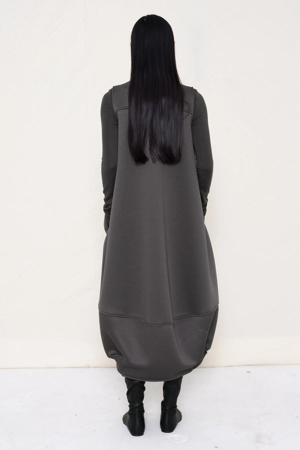 woman-wearing-a-grey-SLEEVELESS-O-LINE-SHAPED-DRESS-WITH-round-POCKETS-over-a-grey-turtle-neck-and-black-leather-pointed-boots-against a-white-background-full-body-back-view