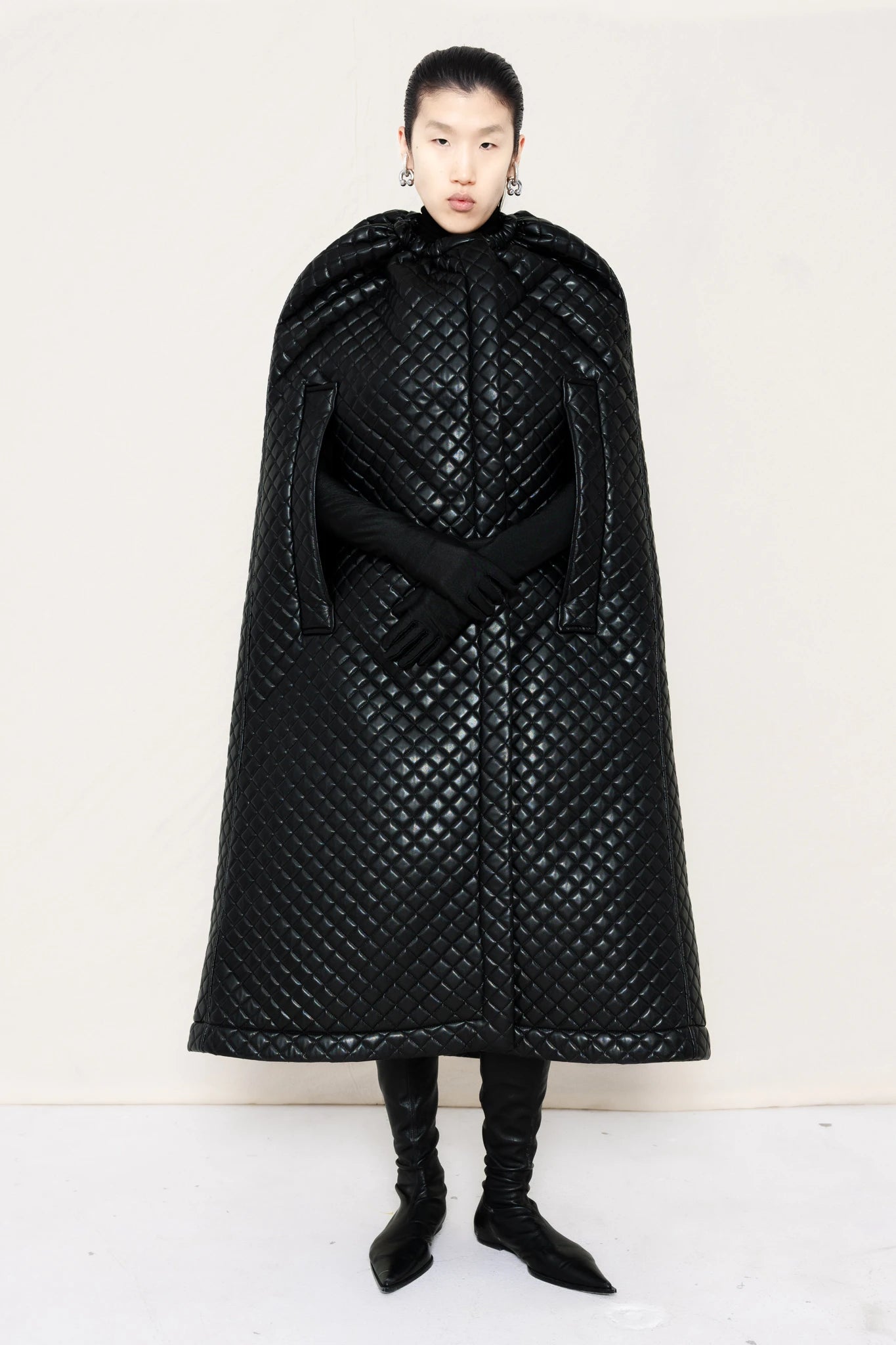 PERSON-WEARING-PIERCED-EARINGS-WITH-BLACK-PLEATHER-QUILTED-CAPE-BLACK-GLOVES-AND-POINTY-FLAT-BLACK-BOOTS-FRONT-VIEW