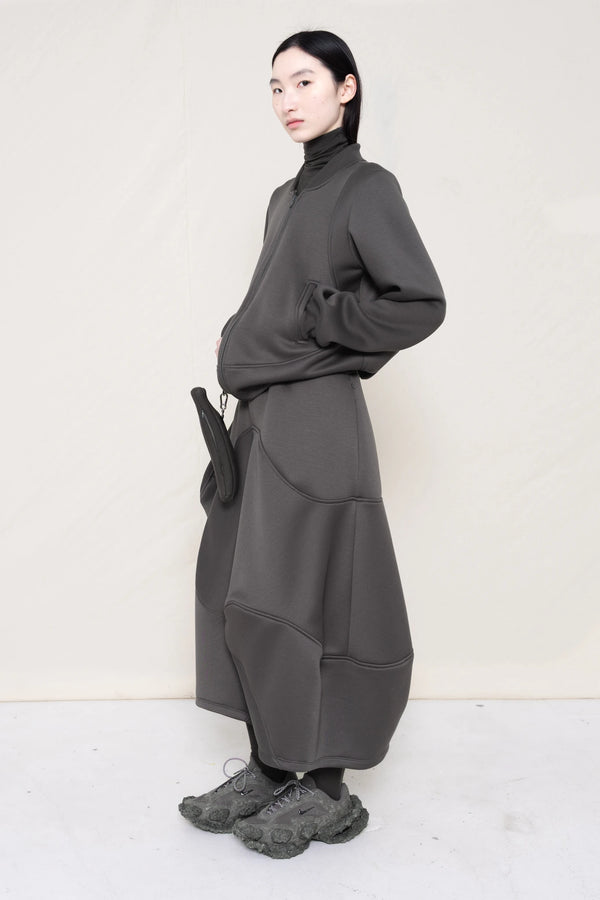 PERSON-WEARING-STONE-GREY-WAVY-ZIP-UP-WITH-MATCHING-WAVY-SEAM-SKIRT-ACCESSORIZED-WITH-CUSTOM-SNEAKERS-AND-GREY-BANANA-TOTE-BAG-THREE-QUARTER-VIEW