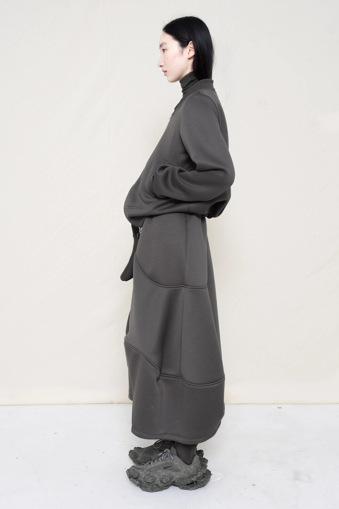 PERSON-WEARING-STONE-GREY-WAVY-ZIP-UP-WITH-MATCHING-WAVY-SEAM-SKIRT-ACCESSORIZED-WITH-CUSTOM-SNEAKERS-AND-GREY-BANANA-TOTE-BAG-SIDE-VIEW