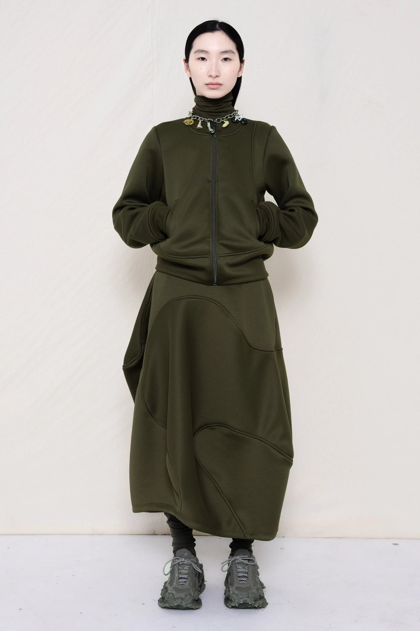 PERSON-WEARING-MOSS-WAVY-ZIP-UP-WITH-MATCHING-WAVY-SEAM-SKIRT-ACCESSORIZED-WITH-MB-CHARM-NECKLACE-AND-CUSTOMIZED-SNEAKERS-FRONT-VIEW