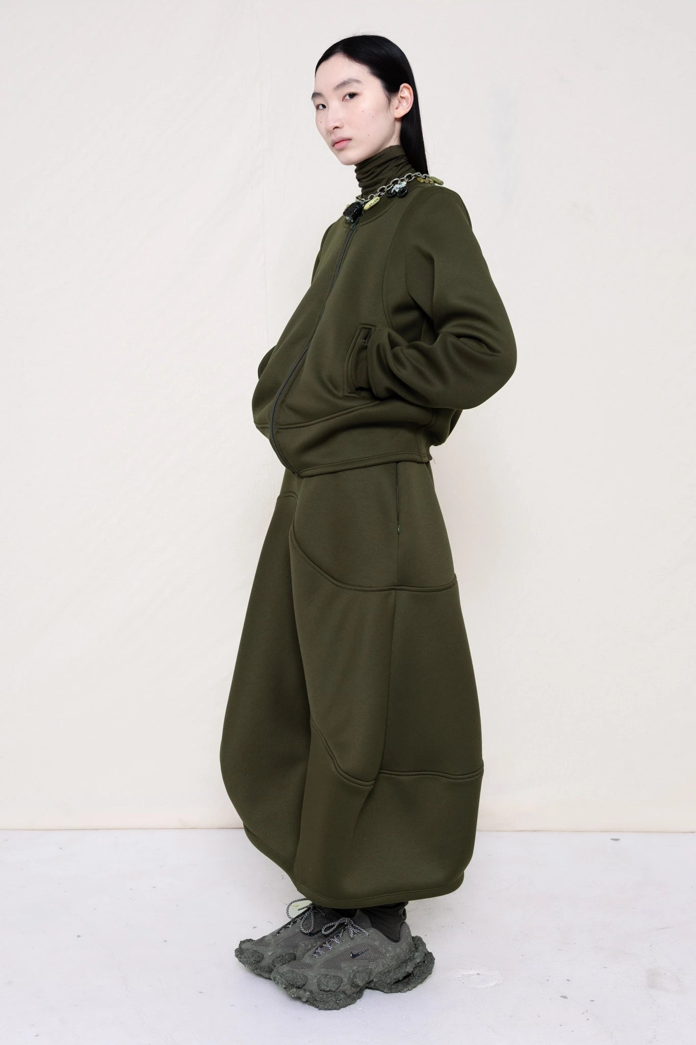 PERSON-WEARING-MOSS-WAVY-ZIP-UP-WITH-MATCHING-WAVY-SEAM-SKIRT-ACCESSORIZED-WITH-MB-CHARM-NECKLACE-AND-CUSTOMIZED-SNEAKERS-THREE-QUARTER-VIEW