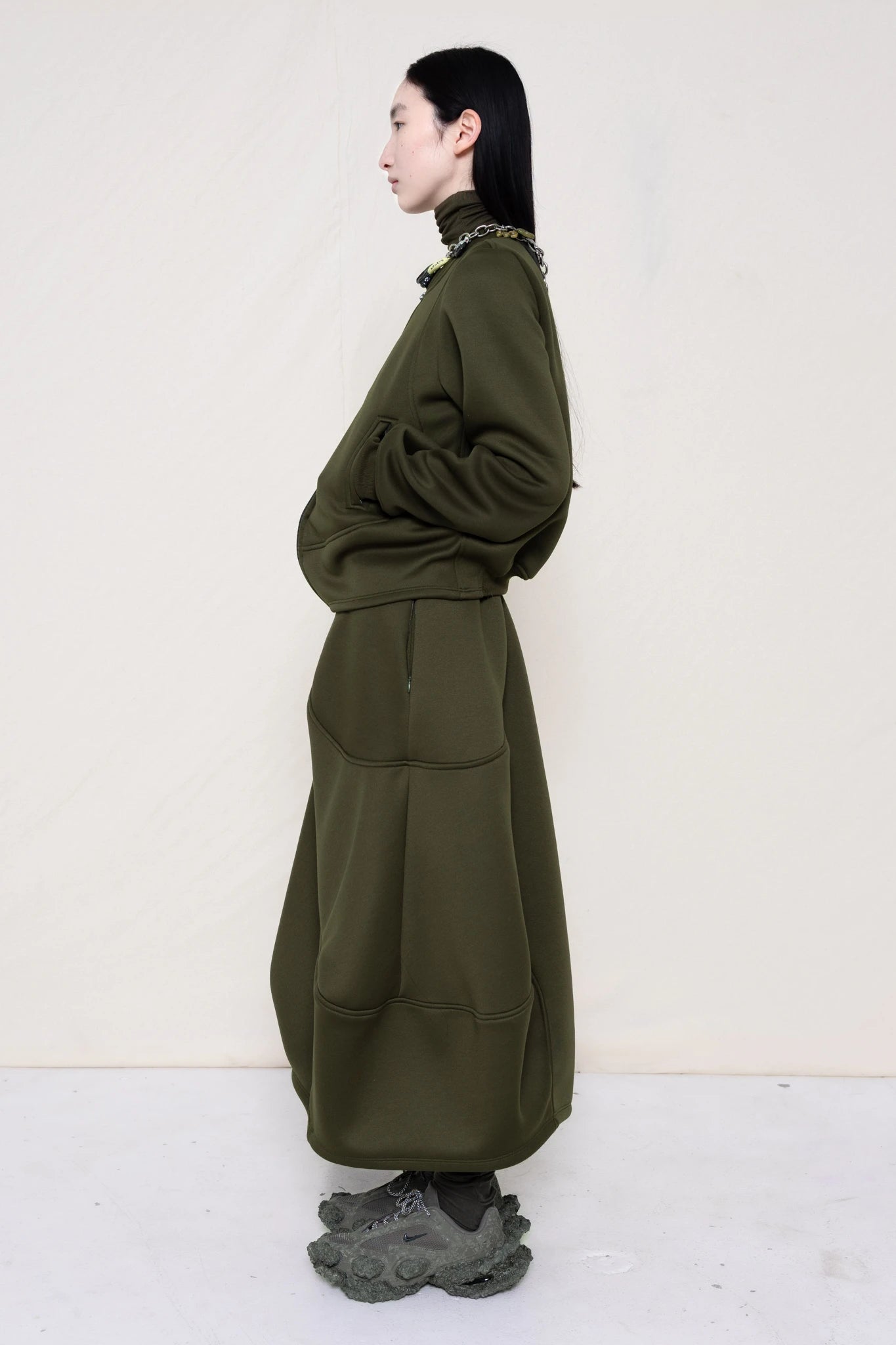 PERSON-WEARING-MOSS-WAVY-ZIP-UP-WITH-MATCHING-WAVY-SEAM-SKIRT-ACCESSORIZED-WITH-MB-CHARM-NECKLACE-AND-CUSTOMIZED-SNEAKERS-SIDE-VIEW
