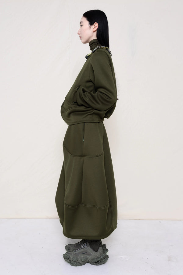 PERSON-WEARING-MOSS-WAVY-ZIP-UP-WITH-MATCHING-WAVY-SEAM-SKIRT-ACCESSORIZED-WITH-MB-CHARM-NECKLACE-AND-CUSTOMIZED-SNEAKERS-SIDE-VIEW