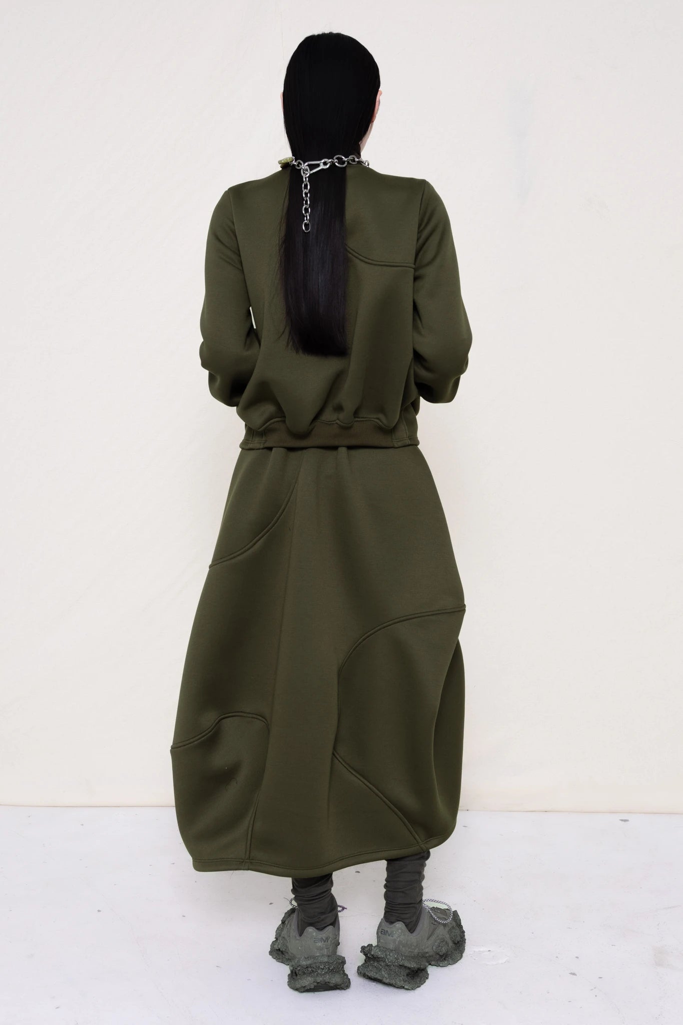 PERSON-WEARING-MOSS-WAVY-ZIP-UP-WITH-MATCHING-WAVY-SEAM-SKIRT-ACCESSORIZED-WITH-MB-CHARM-NECKLACE-AND-CUSTOMIZED-SNEAKERS-BACK-VIEW