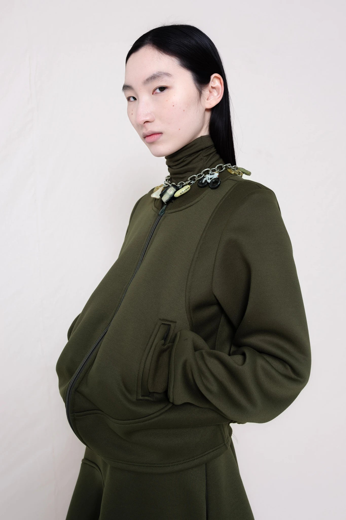 PERSON-WEARING-MOSS-WAVY-ZIP-UP-WITH-MATCHING-WAVY-SEAM-SKIRT-ACCESSORIZED-WITH-MB-CHARM-NECKLACE-CLOSE-UP-THREE-QUARTER-VIEW