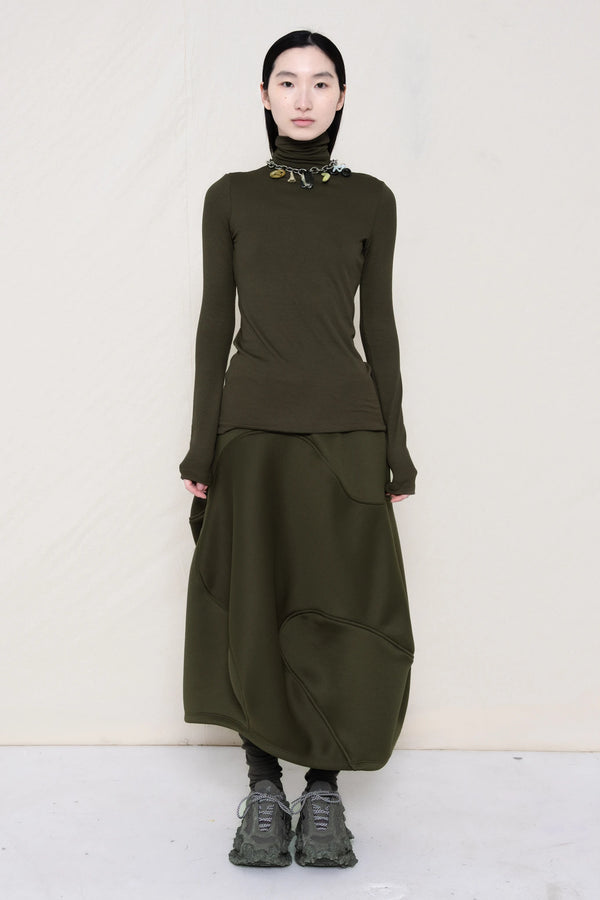 woman-wearing-a-cold-moss-green-soft-fluid-rib-long-sleeve-turtleneck-with-an-mb-charm-necklace-over-a-moss-green-spongy-seamed-skirt-and-custom-shoes-against-a-white-background-full-body-front-view