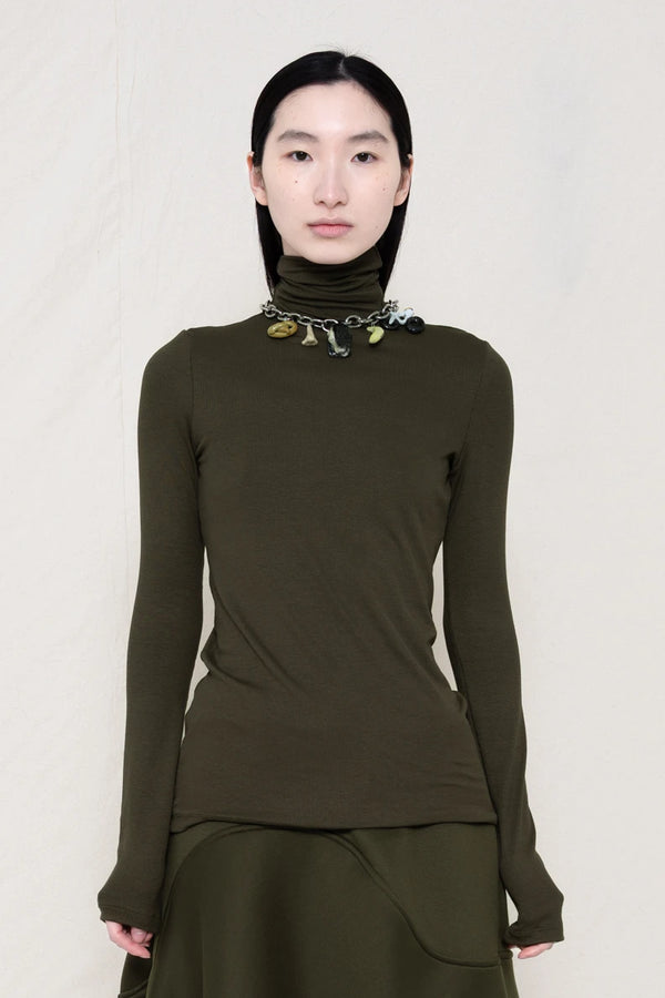 woman-wearing-a-cold-moss-green-soft-fluid-rib-long-sleeve-turtleneck-with-an-mb-charm-necklace-over-a-moss-green-spongy-seamed-skirt-against-a-white-background-front-view