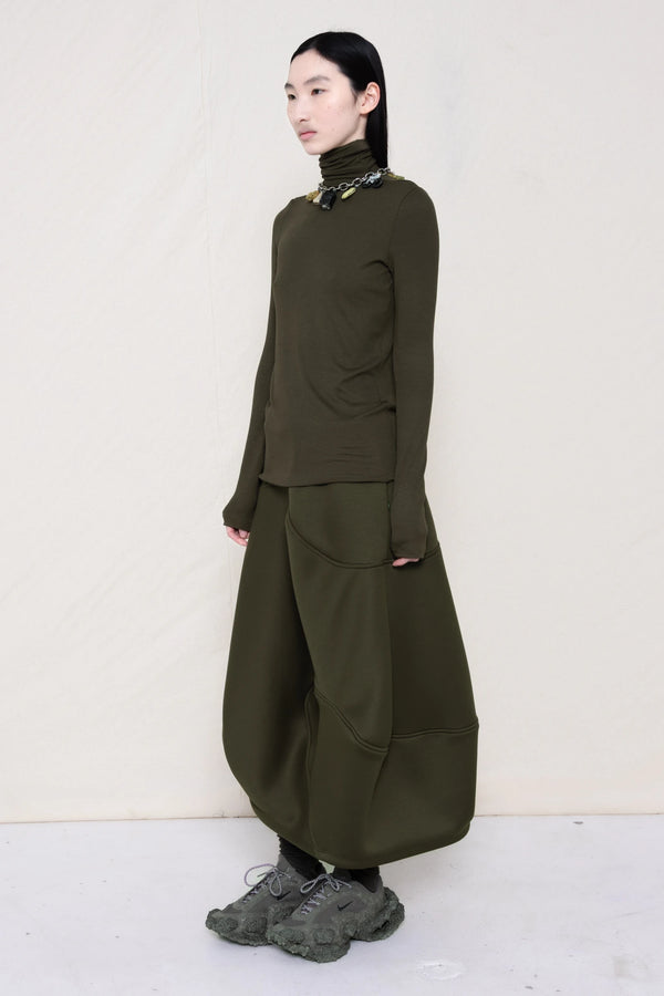 woman-wearing-a-cold-moss-green-soft-fluid-rib-long-sleeve-turtleneck-with-an-mb-charm-necklace-over-a-moss-green-spongy-seamed-skirt-and-custom-shoes-against-a-white-background-full-body-three-quarter-view