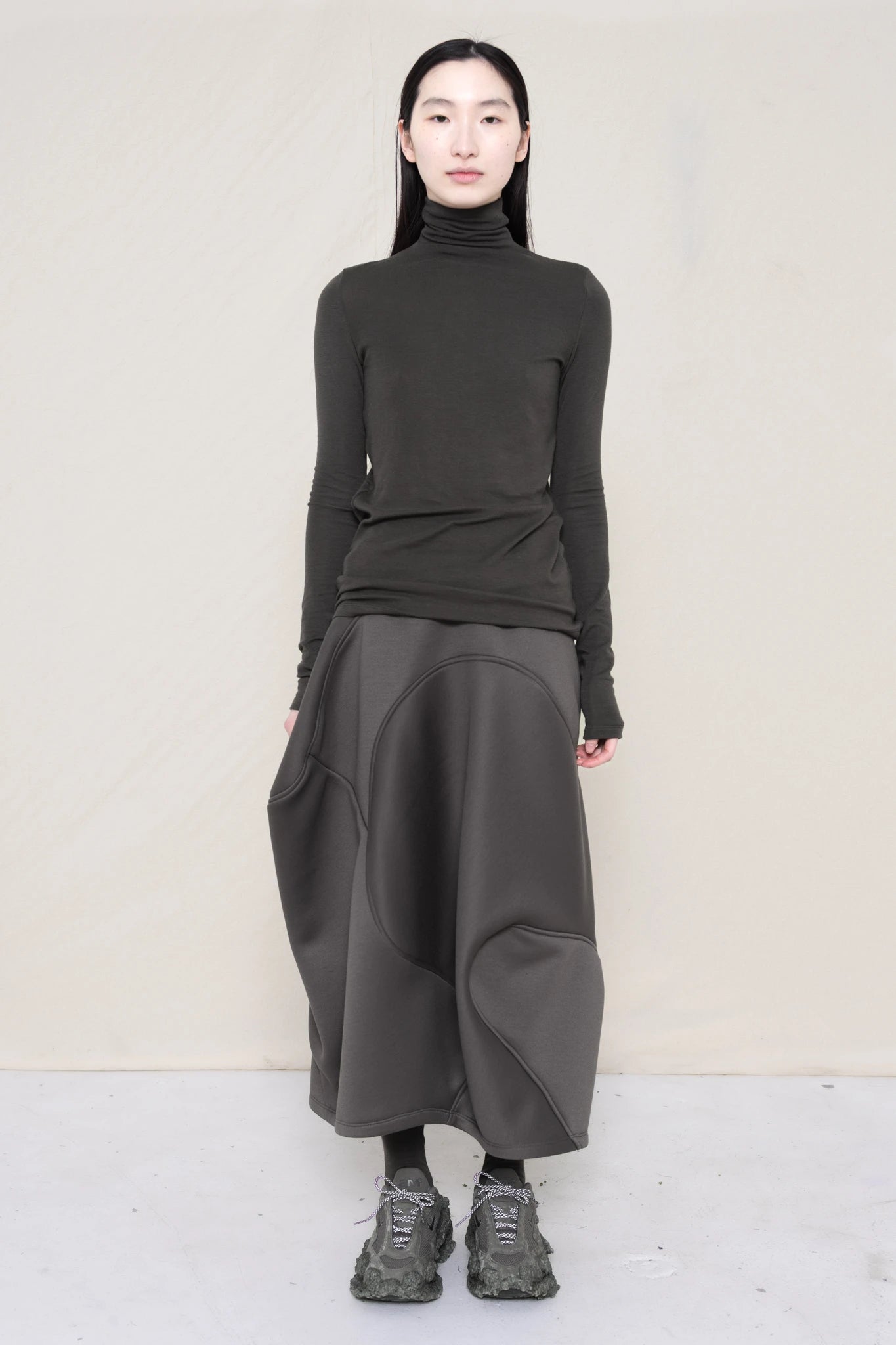 PERSON-WEARING-WARM-GREY-LONG-SLEEVE-TURTLENECK-WITH-STONE-GREY-WAVY-SEAM-SKIRT-AND-CUSTOMIZED-SNEAKERS-FRONT-VIEW