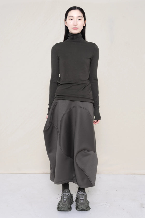 woman-wearing-a-warm-grey-soft-fluid-rib-long-sleeve-turtleneck-with-an-mb-charm-necklace-over-a-grey-spongy-seamed-skirt-and-custom-shoes-against-a-white-background-full-body-front-view