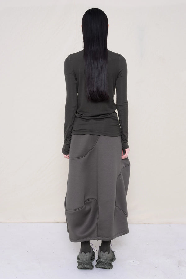 woman-wearing-a-warm-grey-soft-fluid-rib-long-sleeve-turtleneck-with-an-mb-charm-necklace-over-a-grey-spongy-seamed-skirt-and-custom-shoes-against-a-white-background-full-body-back-view