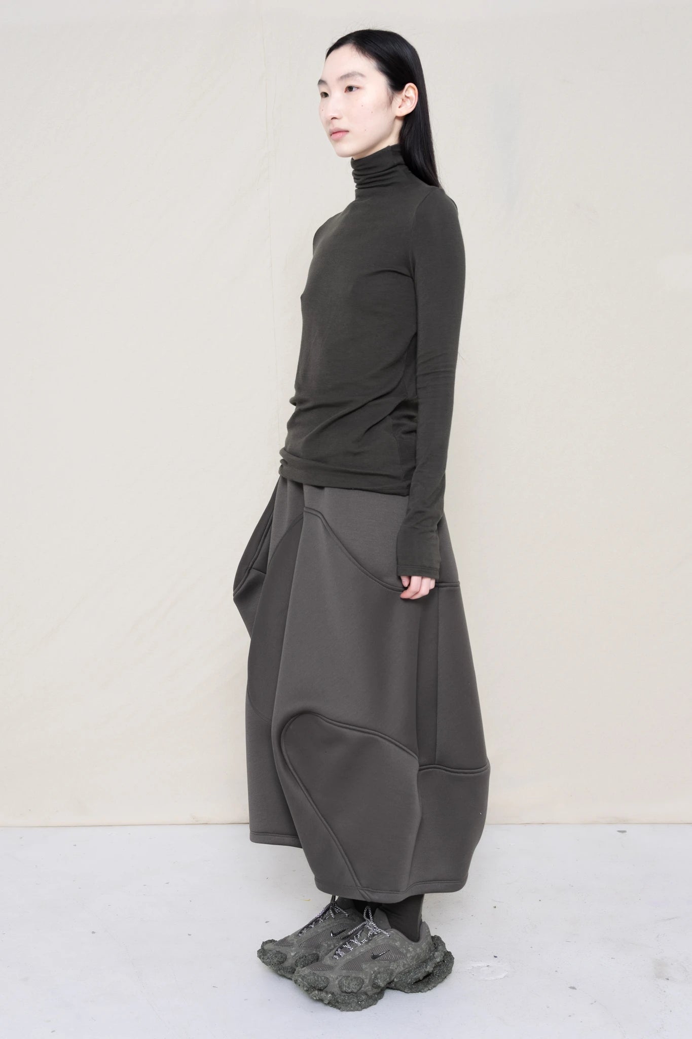 PERSON-WEARING-WARM-GREY-LONG-SLEEVE-TURTLENECK-WITH-STONE-GREY-WAVY-SEAM-SKIRT-AND-CUSTOMIZED-SNEAKERS-THREE-QUARTER-VIEW