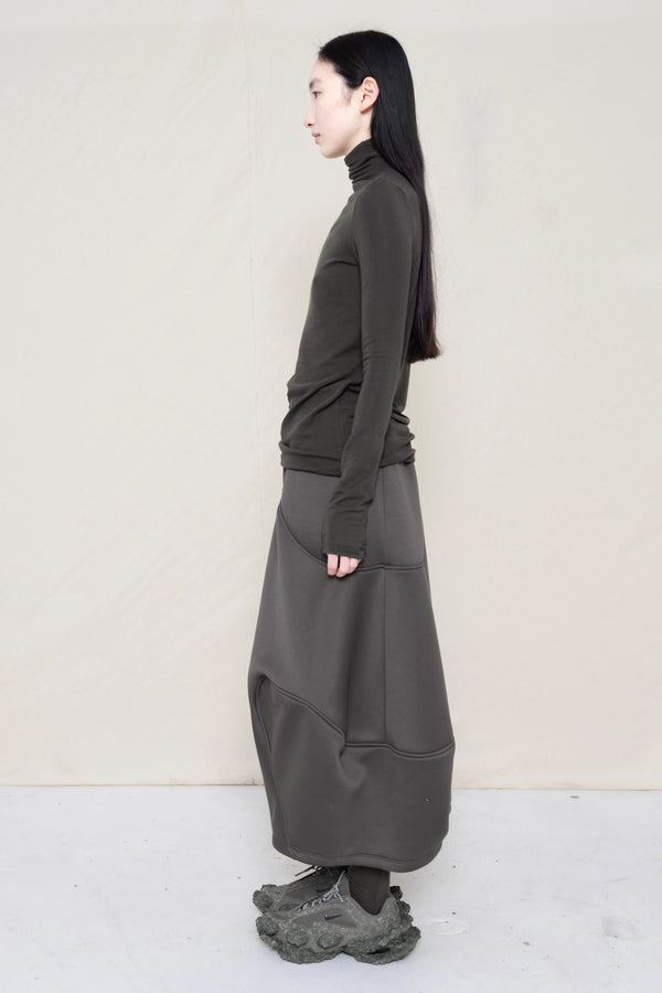 woman-wearing-a-warm-grey-soft-fluid-rib-long-sleeve-turtleneck-with-an-mb-charm-necklace-over-a-grey-spongy-seamed-skirt-and-custom-shoes-against-a-white-background-full-body-side-view