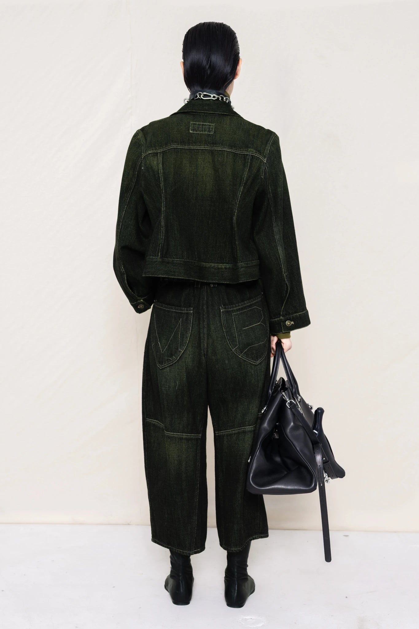 PERSON-WEARING-PIERCED-CHOKER-ON-MOSS-LONG-SLEEVE-TURTLENECK-UNDER-CROPPED-BLACK-YELLOW-WASH-SOFT-DENIM-JACKET-WITH-MATCHING-PANTS-HOLDING-A-LINE-SHOPPER-BACK-VIEW