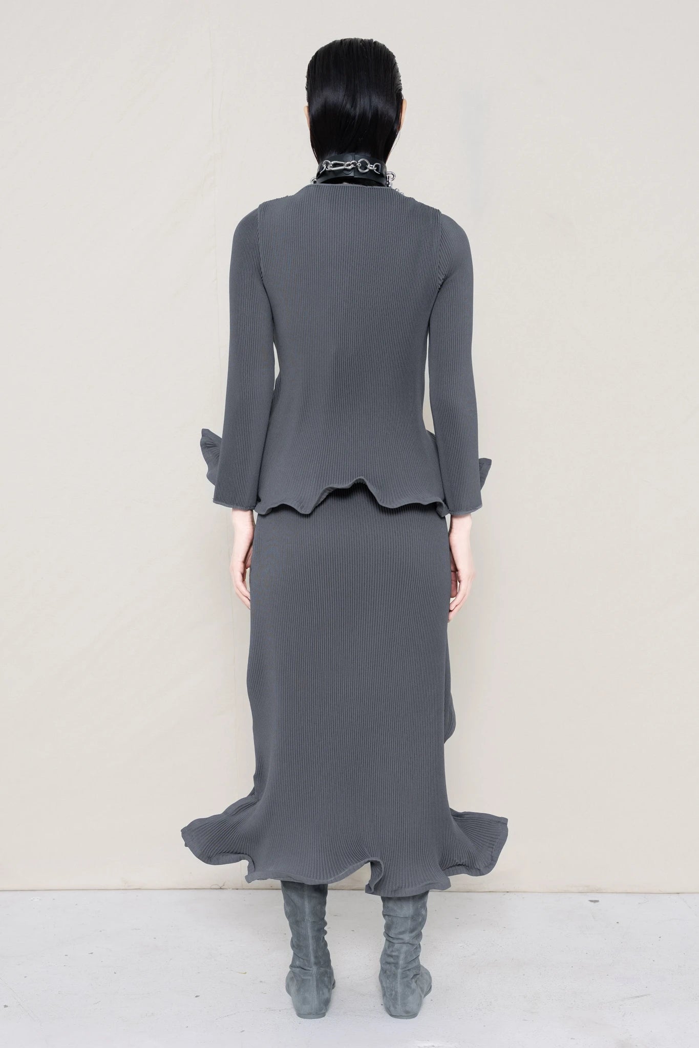 PERSON-WEARING-COLD-GREY-RIPPLE-PLEAT-ZIG-ZAG-HEM-TOP-AND-MATCHING-RIPPLE-PLEAT-ZIG-ZAG-HEM-SKIRT-ACCESSORIZED-WITH-PIERCED-CHOKER-AND-GREY-FLAT-POINTY-BOOTS-BACK-VIEW