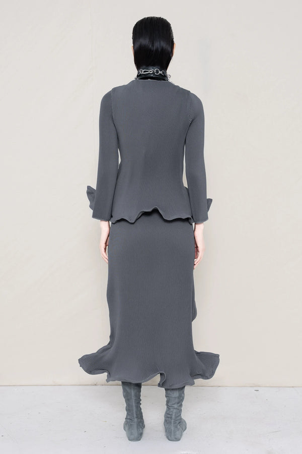 PERSON-WEARING-COLD-GREY-RIPPLE-PLEAT-ZIG-ZAG-HEM-TOP-AND-MATCHING-RIPPLE-PLEAT-ZIG-ZAG-HEM-SKIRT-ACCESSORIZED-WITH-PIERCED-CHOKER-AND-GREY-FLAT-POINTY-BOOTS-BACK-VIEW