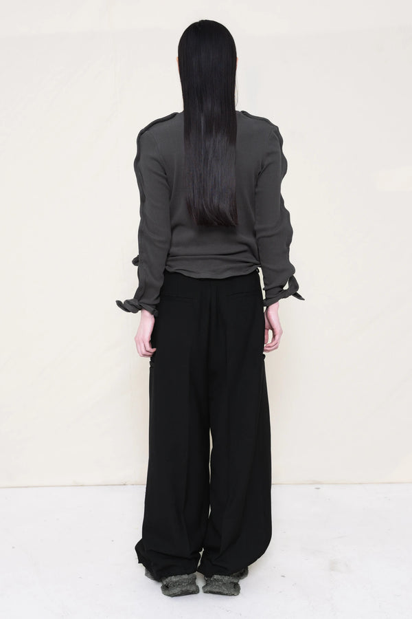 PERSON-WEARING-DARK-GREY-ZIG-ZAG-TOP-FEATURING-MALLEABLE-SLEEVES-PAIRED-WITH-BLACK-TAILORED-PANTS-AND-CUSTOMIZED-SNEAKERS-BACK-VIEW