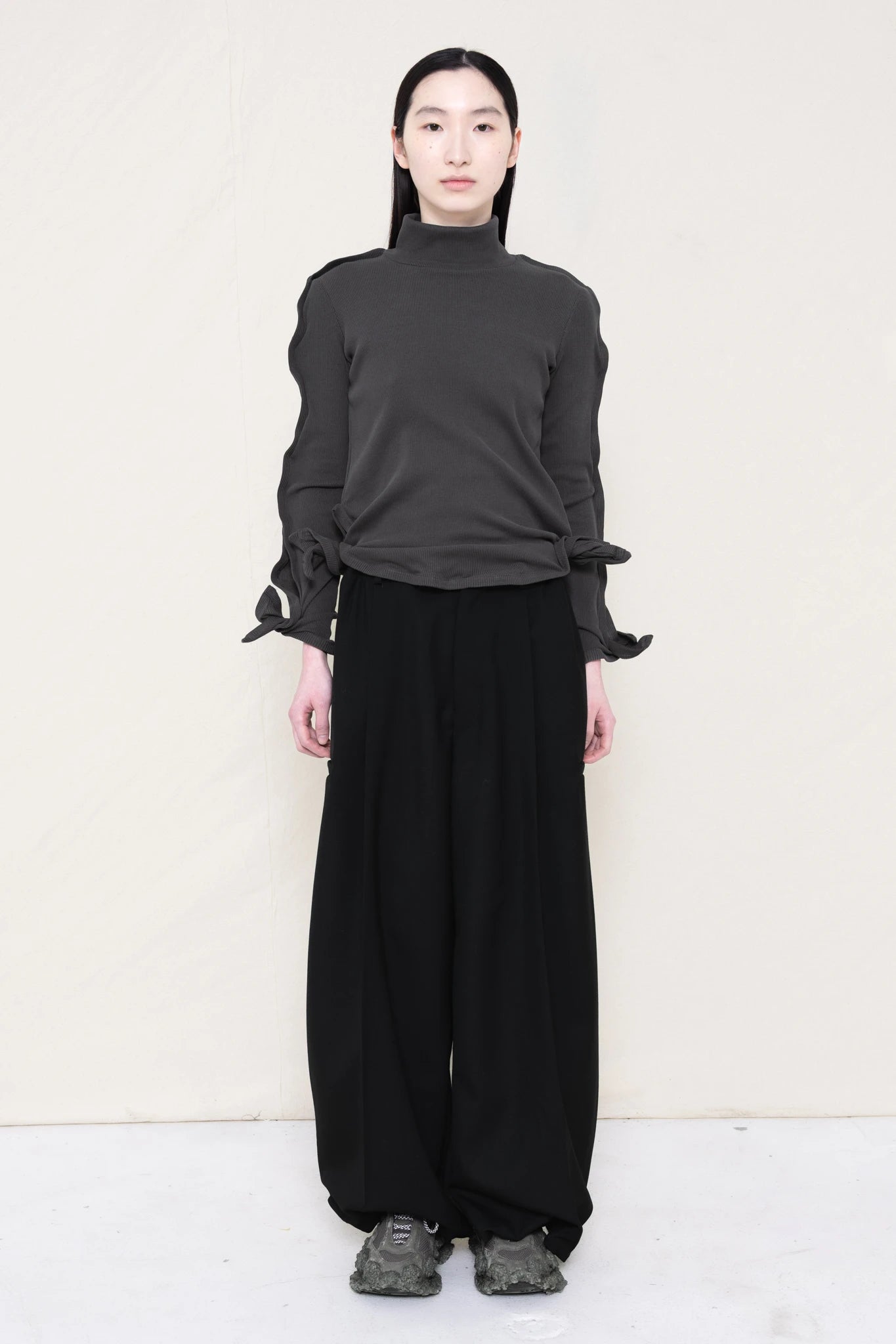 PERSON-WEARING-DARK-GREY-ZIG-ZAG-TOP-FEATURING-MALLEABLE-SLEEVES-PAIRED-WITH-BLACK-TAILORED-PANTS-AND-CUSTOMIZED-SNEAKERS-FRONT-VIEW
