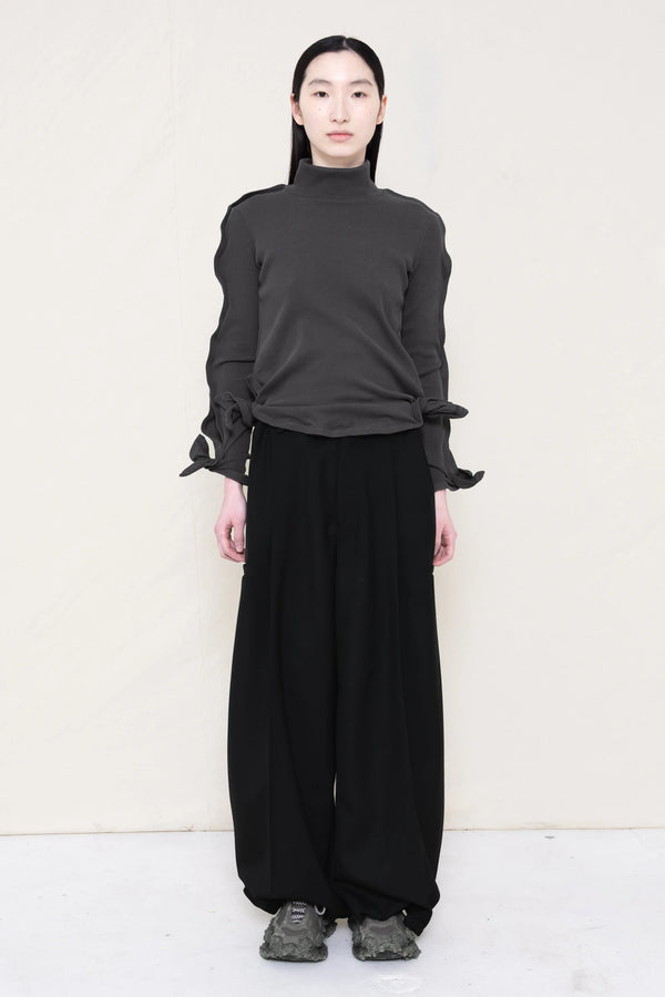PERSON-WEARING-DARK-GREY-ZIG-ZAG-TOP-FEATURING-MALLEABLE-SLEEVES-PAIRED-WITH-BLACK-TAILORED-PANTS-AND-CUSTOMIZED-SNEAKERS-FRONT-VIEW