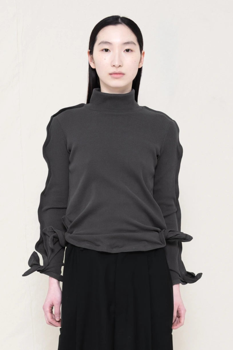 PERSON-WEARING-DARK-GREY-ZIG-ZAG-TOP-FEATURING-MALLEABLE-SLEEVES-PAIRED-WITH-BLACK-TAILORED-PANTS-CLOSE-UP-FRONT-VIEW